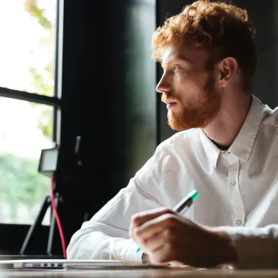 Man kijkt uit het raam en houdt pen vast
